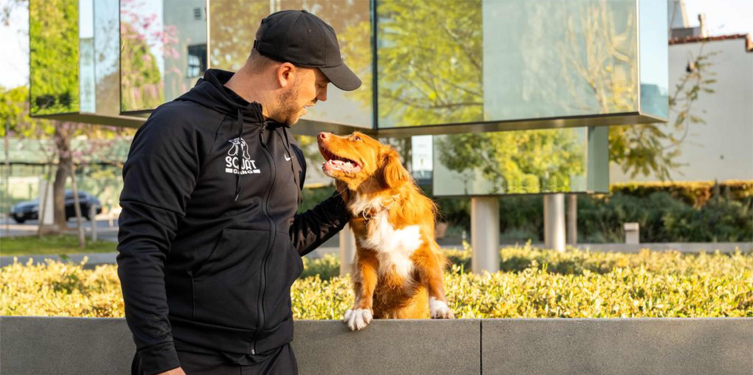 Man in a black jacket interacts affectionately with a brown dog outdoors.